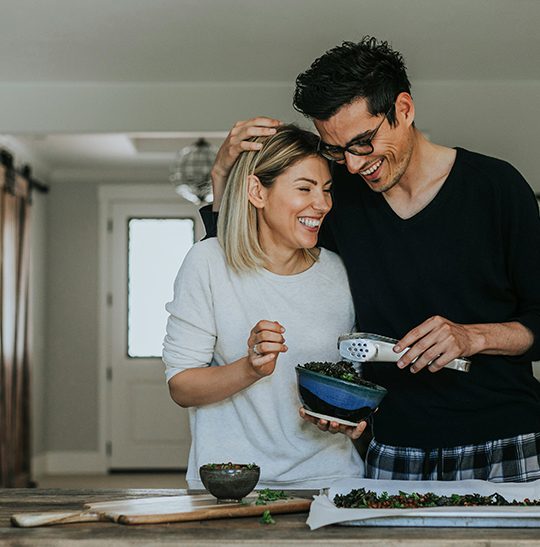 Couple laughing together while preparing meal at home.