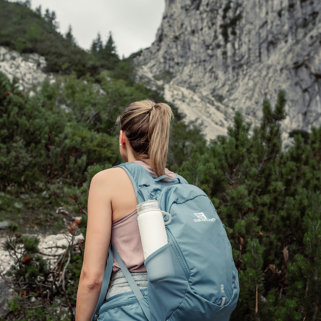Person with backpack hiking in rocky, mountainous terrain.