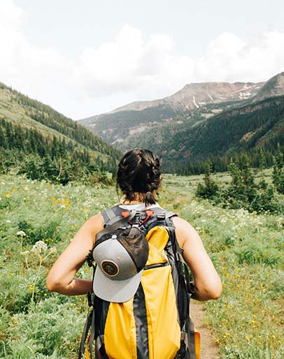 Person with backpack hiking through grassy, mountainous terrain.