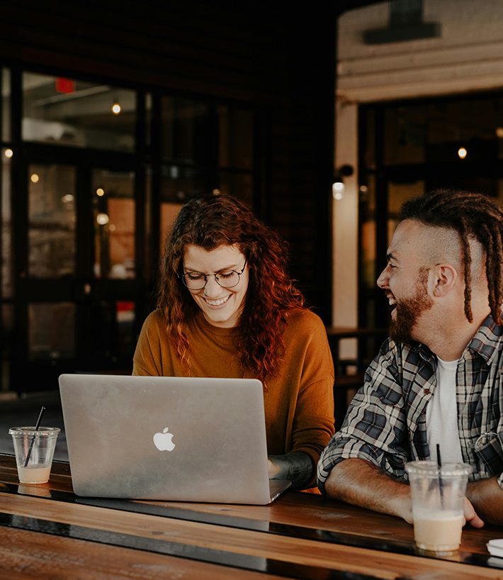 Two friends laughing together and working on laptop computer in coffee shop.