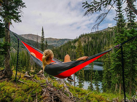 Person relaxing in hammock overlooking mountain lake.