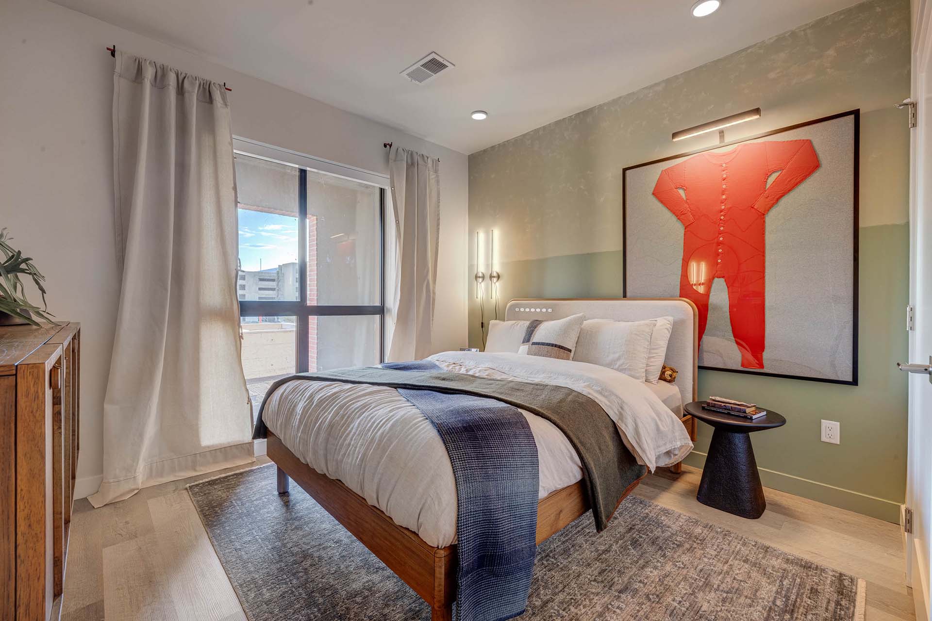Millhaus apartment bedroom with plush bed, large window, and eclectic decor.