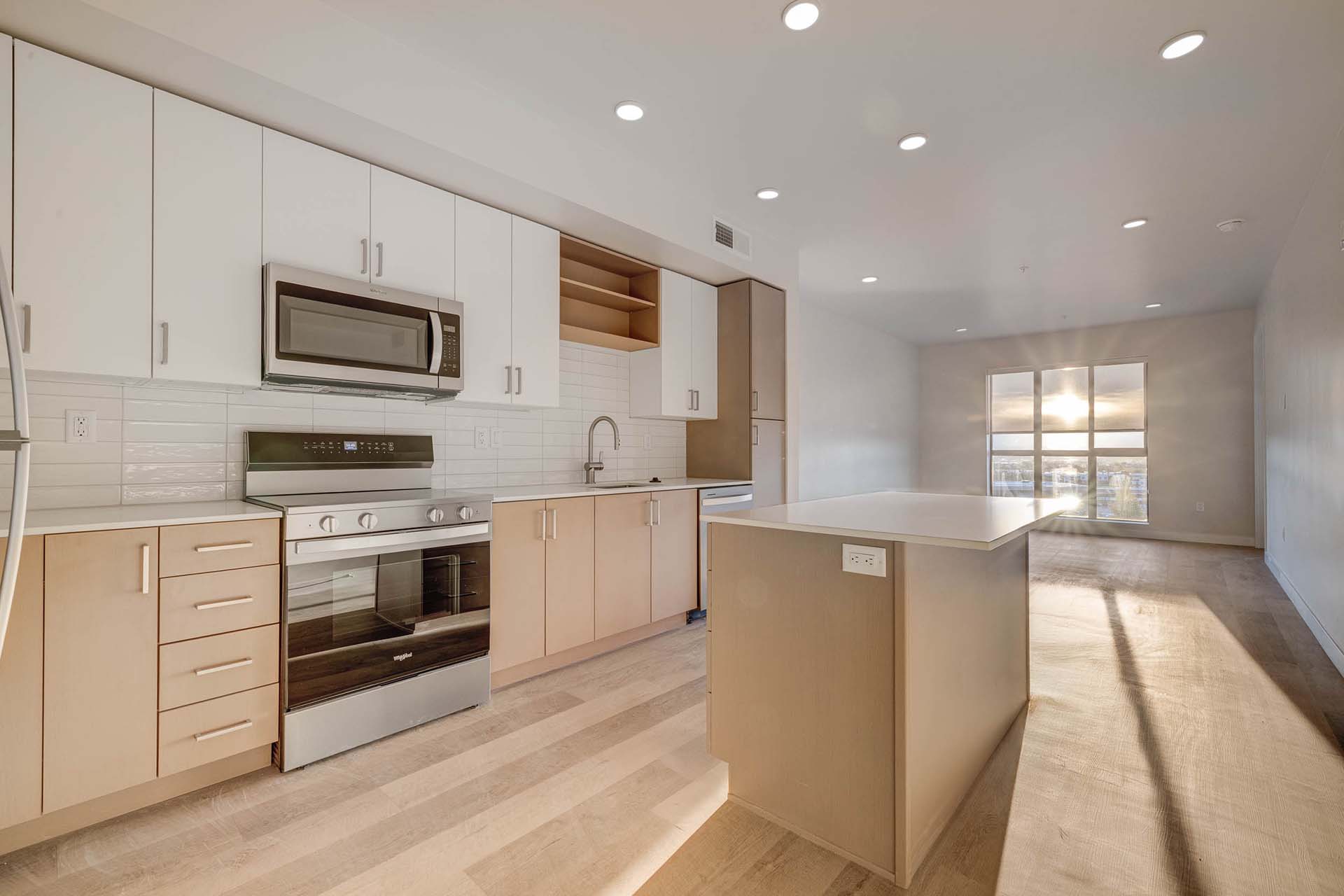 Millhaus apartment kitchen with wood style floor and cabinets, light counters, and stainless steel appliances.