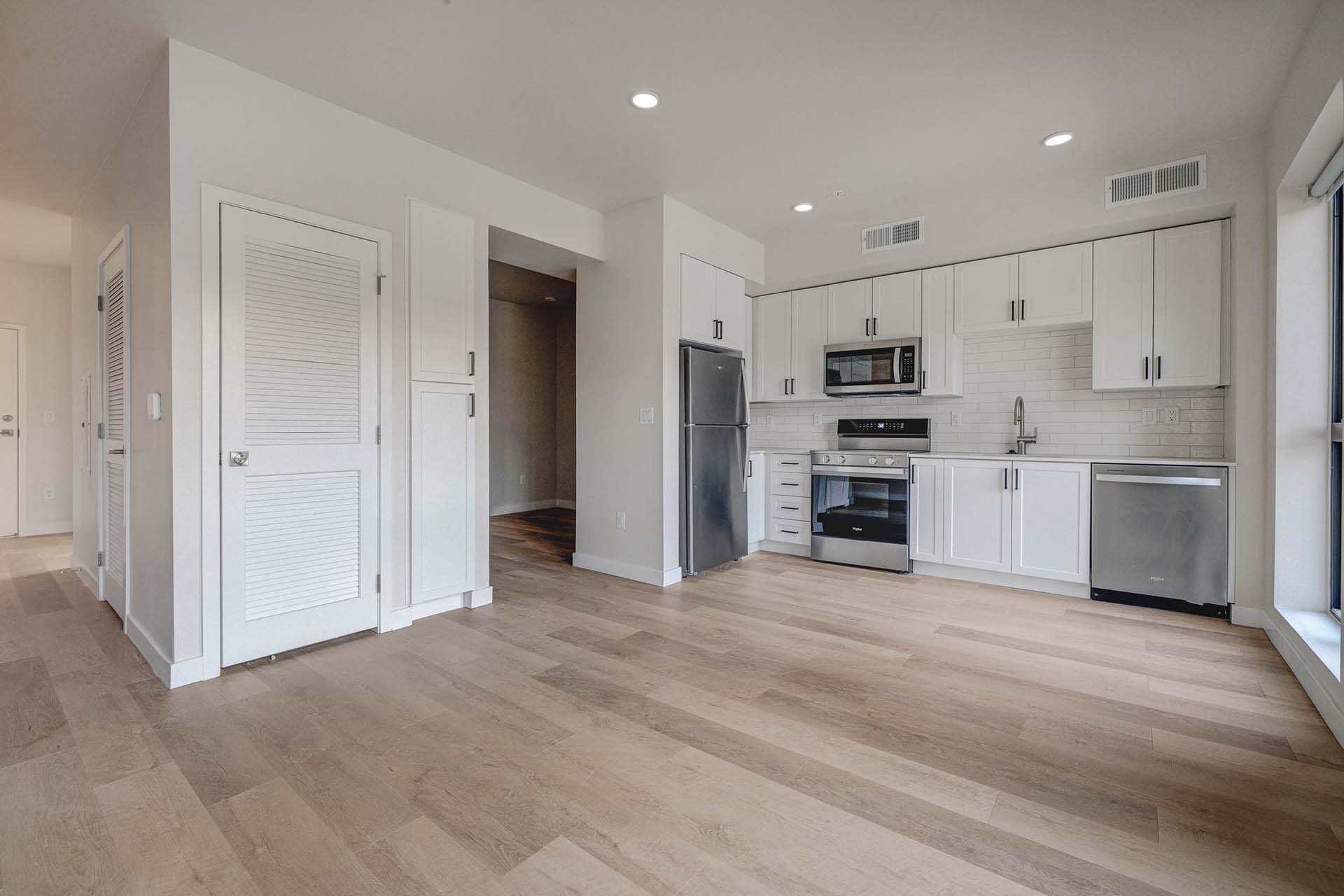 Millhaus apartment kitchen with wood style floor, white cabinets, and stainless steel appliances.