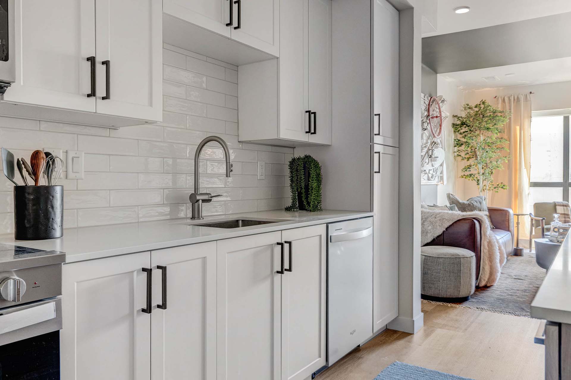 Millhaus apartment kitchen with wood style floor, white cabinets, and tiled backsplash.
